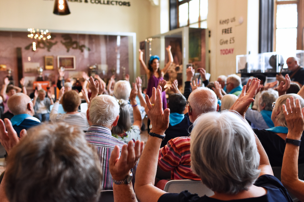 Elderly visitors in The Beaney galleries with their arms in the air, participating in a wellbeing workshop