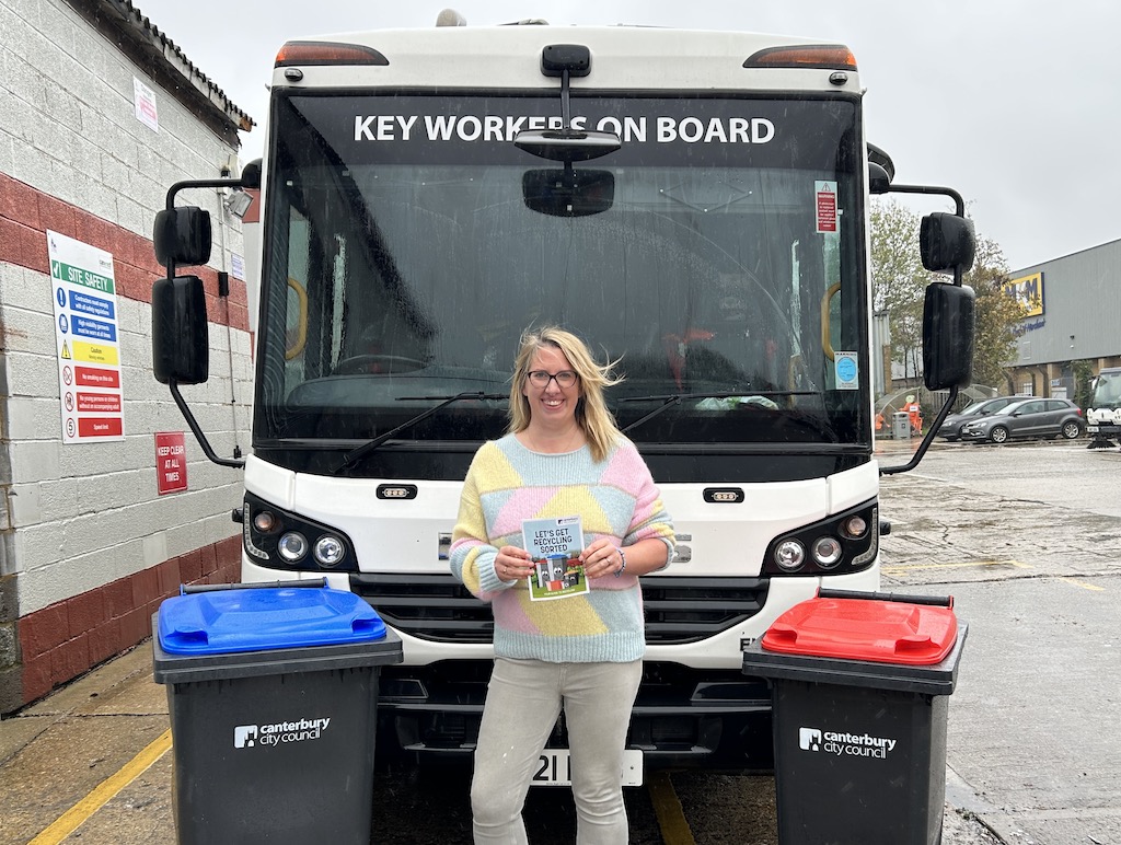 Cllr Charlotte Cornell holding the new recycling guide standing in front of a recycling lorry with a recycling bin either side of her