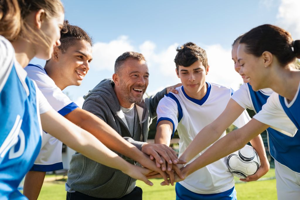 Young people in football kits with their hands together with their coach