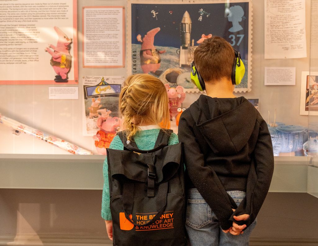 Two children with special educational needs looking at The Beaney's Clangers display case wearing the SEND family backpacks